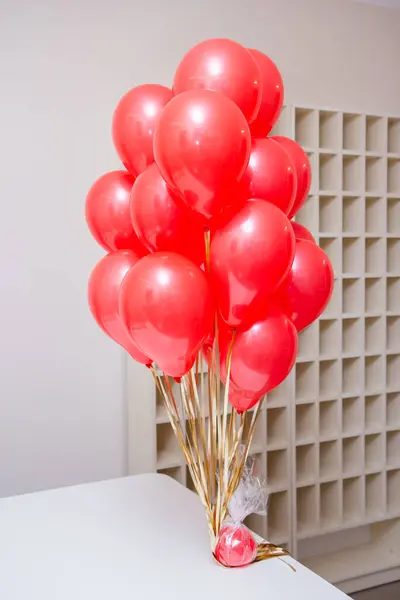 a bunch of small red helium balloons on a white table