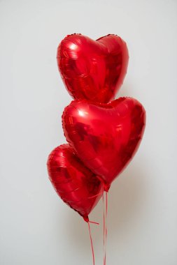 Beyaz arka planda helyum içeren kırmızı kalp balonları.