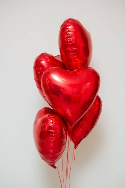 Beyaz arka planda helyum içeren kırmızı kalp balonları.