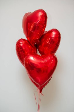 Beyaz arka planda helyum içeren kırmızı kalp balonları.