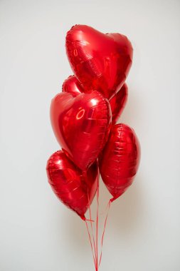 Beyaz arka planda helyum içeren kırmızı kalp balonları.