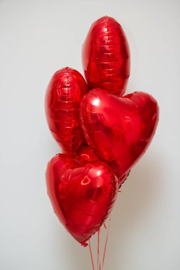 Beyaz arka planda helyum içeren kırmızı kalp balonları.