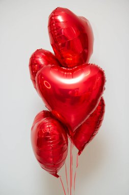 Beyaz arka planda helyum içeren kırmızı kalp balonları.