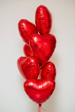 Beyaz arka planda helyum içeren kırmızı kalp balonları.