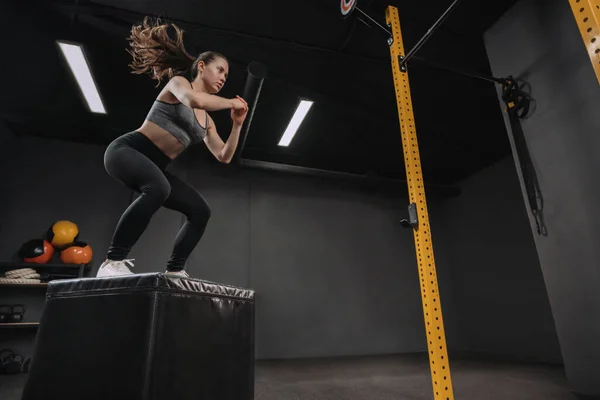 做跳伞运动的女人是她的杂技训练的一部分 女运动员在黑暗的健身房里蹲着 跳到包厢里 复制空间 — 图库照片