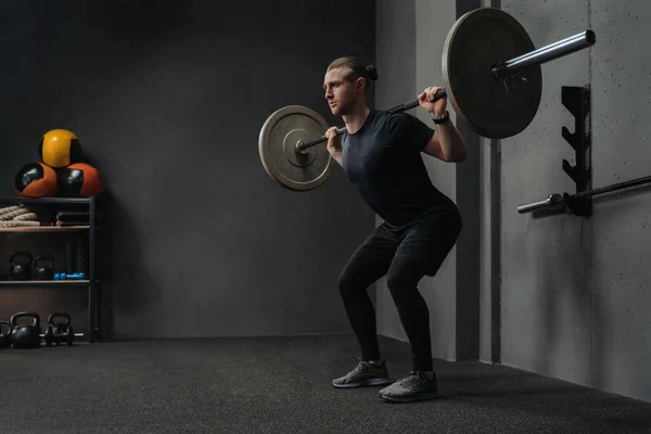 男子解除杠铃作为在黑暗锻炼健身房的交叉组合训练的一部分 案文的篇幅 — 图库照片