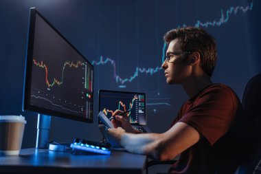 Side view of young man trader analyst at working table, analyzing financial chart, stock quotes, share prices, trading online, checking data on cryptocurrency graph on computer screen, making notes clipart
