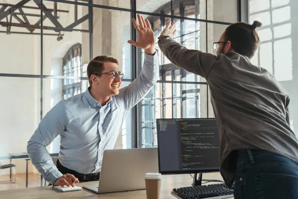 Colleagues coders giving high five to each other celebrating successful start-up launch. Programmers rejoice at the successful launch of their product.