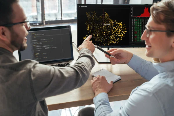 stock image Closeup of two machine learning specialists descanting about new project in office in front of pc, analyzing data. Selective focus on computer screen