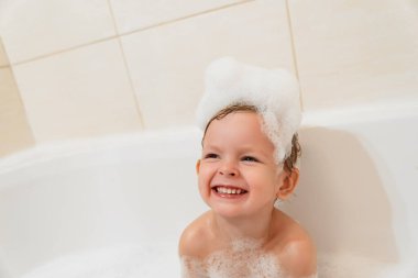 Şirin bir bebek küvette köpükle banyo yapıyor ve gülüyor. Boşluğu kopyala