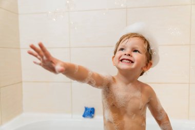Şirin küçük çocuk köpük ve köpüklerle banyoda eğleniyor..