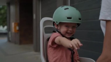 Kask takan neşeli bir çocuk bisiklet koltuğunda oturur ve gezintiden önce eğlenir ve gülümser, dışarıda eğlenir..