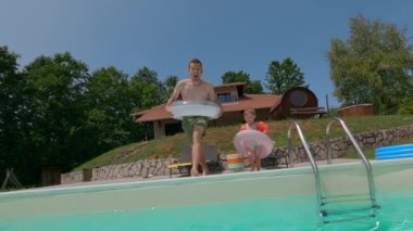 Eğlenceli baba ve küçük oğlu güneşli bir günde şişme yüzüklerle havuza atlayıp neşeli yaz eğlencesinin tadını çıkarıyorlar.. 