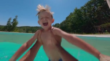 Gülen mutlu küçük bir çocuk babasının kollarına atlıyor ve güneşli bir günde havuzda eğleniyor. POV görünümü