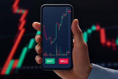 İş adamının elinde, gerçek zamanlı ön bellek ve kripto para birimi grafikleri, takip oranı dalgalanmaları ve piyasa verileri ile ticaret uygulamasını gösteren bir telefon bulunuyor..