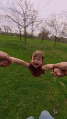 Baba oğullarının ellerini tutuyor, onu parkta bir çember etrafında döndürüyor, neşeli çocuk gülüyor, neşeli anın tadını çıkarıyor, mutlu çocukluk ve aile anılarını birlikte yaratıyor. Dikey video