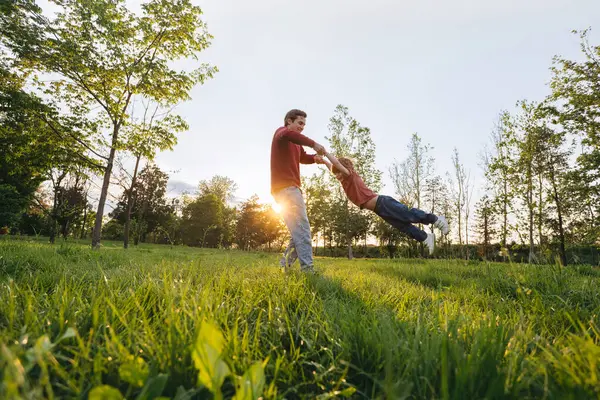 Neşeli genç baba gün batımında mutlu oğlunu çimenli bir parkta döndürüyor. Gülümseyen baba dışarıda neşeli çocuğuyla oynuyor. Aile bağları ve bağları. Metin için boşluk