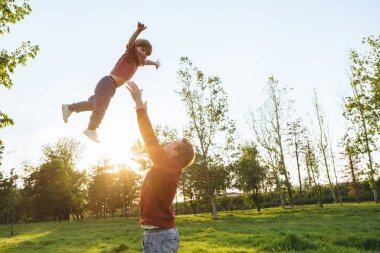 Baba neşeli oğlunu bir parkta havaya fırlatıyor, gülen çocuk güneşli bir yaz gününde babasıyla dışarıda eğleniyor. Aile eğlencesi, bağlanma ve Babalar Günü konsepti. Boşluğu kopyala