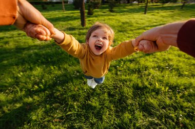 POV bakış açısı, ebeveyn mutlu gülen çocuklarının ellerini tutar ve onu parkta bir çember etrafında döndürür. Baba dışarıda neşeli oğluyla oynuyor. Mutlu çocukluk kavramı