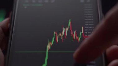 Kullanıcı finansal piyasaları ve fiyat hareketini izlediği için hisse senedi ve kripto grafikleriyle ticaret arayüzünü gösteren cep telefonu ekranını kapat.
