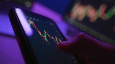 Kapat, iş adamı akıllı telefonda borsa veya kripto para birimi grafiklerini neon ışık altında kullanarak ticaret uygulaması kullanıyor. Telefondaki şifreli trendleri analiz eden tüccar