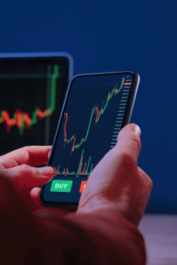 Yakın çekim, akıllı telefonu ticaret uygulaması ile tutan tüccar elleri, mobil ekranda dijital borsa grafikleriyle etkileşime geçiyor. Kripto piyasasına yatırım, analiz ve ticaret. 