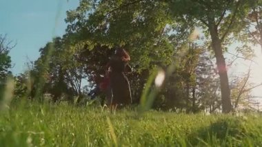 Neşeli anne, parkta yemyeşil çimenler ve ağaçlarla çevrili küçük çocuğunu bir çember içinde döndürür. Mutlu anne dışarıda oynarken oğlunun etrafında dönüyor. Tasasız çocukluk ve aile bağı kavramı.