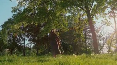 Neşeli genç anne gün batımında mutlu oğlunu çimenli bir parkta döndürüyor. Gülümseyen anne dışarıda neşeli çocuğuyla oynuyor. Aile bağı, bağlanma ve anneler günü konsepti. Yavaş çekim