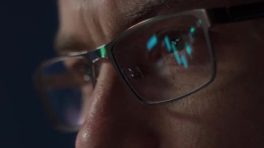 Gözlük takan odaklı kripto tüccarı yakından inceler kripto para birimi veya borsa verilerini şamdan grafikleri ve finansal grafiklerle analiz eder, kripto eğilimlerini izler. 