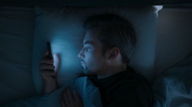 Yakından bakınca, yorgun bir adam gece geç saatlerde sosyal medyayı izlerken uykusuzluk, endişe ve aşırı düşünmeyle boğuşan cep telefonuyla durmadan kaydırıyor. Akıllı telefon bağımlılığı. Üst görünüm