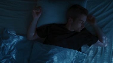 Genç bir adam, uykusuzluk, bıkkınlık ve yorgunluk, aşırı düşünme ve uyku sorunlarıyla boğuşarak huzursuz bir şekilde gece yatağında yatıyor. Üst görünüm, zaman aşımı