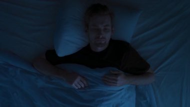Zaman atlaması, endişeli genç bir adam uykusuzluktan muzdarip, yatakta dönüşüyor, gece uyku bozukluğu sırasında uyumaya çalışıyor. Üst görünüm