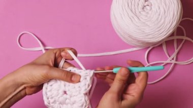 Kadın elinin pembe arka planda kurdele ipliğiyle tığ işi yapması. Yüksek kalite 4k görüntü