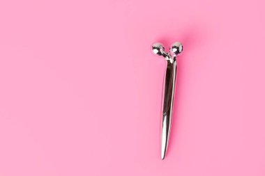 Pastel pembe arka planda fotokopi alanı olan modaya uygun bir yüz masajcısının üst görüntüsü. Cilt bakımı kavramı