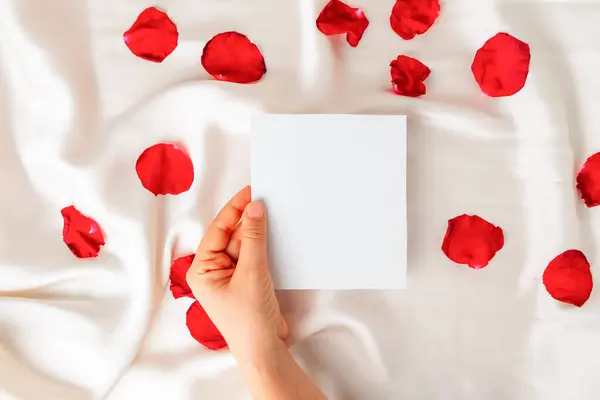 Üst görünümde beyaz saten düz arkaplan üzerinde boş bir nota tutarken fotokopi alanı kullanılıyor. Romantik mesaj konsepti