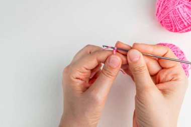 El ele tutuşan pembe iplik ve arka planda roket kancası. Sihirli yüzüğün nasıl örüleceğini öğreten, beşinci adım.