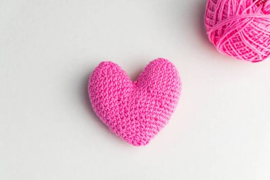 Örgü işi pembe kalp, arka planda iplik yumağı, üst manzara.