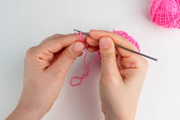 El ele tutuşan pembe iplik ve arka planda roket kancası. Sihirli yüzüğün nasıl örüleceği üzerine ders, adım 3