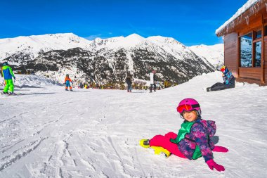 Young skier, a child, sitting on the snow, a ski slope, smiling and looking at camera. Winter holidays in El Tarter, Andorra, Pyrenees Mountains