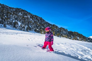 Smiling girl standing in deep fresh snow powder in a ski gear with mountains and forest in a background. Winter ski holidays, Andorra, Pyrenees