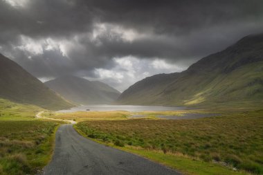 Road leading trough Doolough Valley with lakes, between Glenummera and Glencullin mountain ranges with dark dramatic sky, Mayo, Ireland