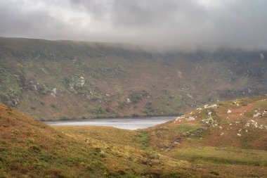 Lake, Lough Bray tepelerin ve uçurumların arkasında saklanıyor, dramatik fırtına bulutları ve gökyüzüyle çevrili. Wicklow Dağları 'nda yürüyüş, İrlanda