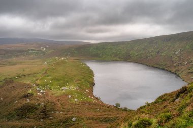 Lake, Lough Bray 'in solunda dağ izleri ve sağında kayalıklar var. Huysuz, dramatik fırtına bulutlarıyla kaplı. Wicklow Dağları 'nda yürüyüş, İrlanda