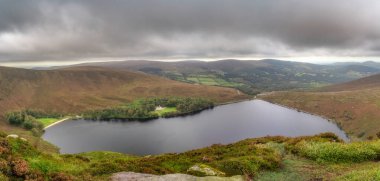 Lough Bray Gölü 'nün panoramik manzarası. Evi, küçük ormanı ve plajı dramatik fırtına bulutlarıyla çevrili. Wicklow Dağları 'nda yürüyüş, İrlanda