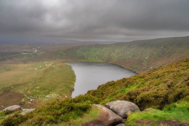 Tepenin tepesinden Lough Bray gölünün manzarası karamsar, dramatik fırtına bulutlarıyla kaplı. Wicklow Dağları 'nda yürüyüş, İrlanda