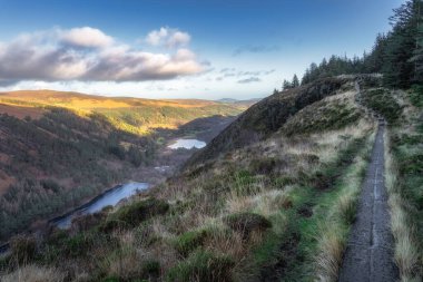 Dağın tepesindeki tahta kaldırımda Glendalough gölleri ve ormanı manzaralı. Güzel sonbahar Wicklow Dağlarında yürüyüş, İrlanda