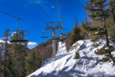 People riding up on a ski lift to hit early slopes covered in fresh snow, Montgenevre ski village on border of France and Italy. Winter sport in Alps clipart