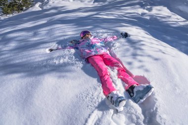 Kayak ekipmanlı genç bir kız, dağlarda kar meleği gibi gülümsüyor ve kar meleği yapıyor, Montgenevre kayak köyü, Fransa, Alpler