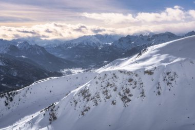 Montgenevre kayak köyü, Fransa 'nın Alpleri' nde, dramatik ve değişken bir gökyüzü altında görkemli bir şekilde yükselen engin, karla kaplı tepeleri ve görkemli sıradağları gösteren nefes kesici bir kış manzarası.