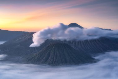 Şafak vakti Bromo yanardağının bulutların üzerinde yükselmesini, Endonezya 'nın şaşırtıcı volkanik güzelliğini ve çeşitli doğal manzaralarını, Doğu Java, Endonezya' yı gözlemleyin.